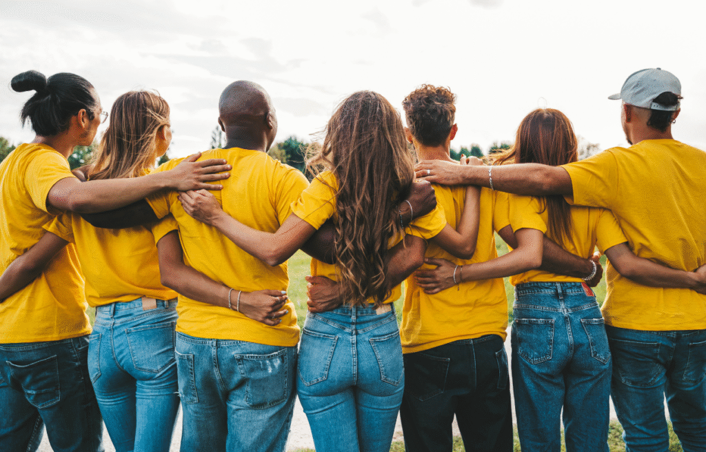 Sieben Personen stehen nebeneinander und haben sich im Arm